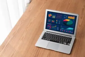 Laptop on a wooden desk displaying a colorful data analytics dashboard on its screen.