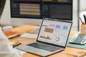 Laptop on a wooden desk displaying a colorful analytics dashboard with charts and graphs on screen.