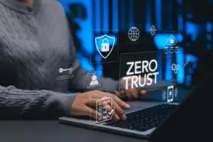 Person typing on a laptop with floating security icons and a prominent 'ZERO TRUST' label, illustrating cybersecurity.