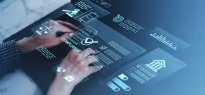 Person’s hands interact with a transparent touch screen displaying charts, graphs, and data icons on a blue-toned dashboard.