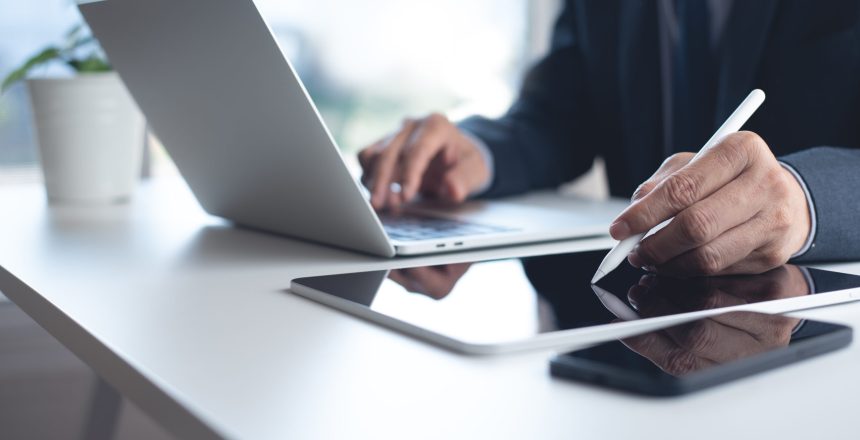 Closeup of businessman using stylus pen on digital tablet and working on laptop computer with mobile smart phone on office table