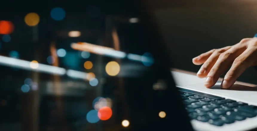 young man hand working on a laptop, bokeh blurred at night For text copy space, image size horizontal.