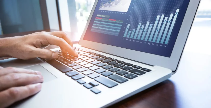 Person typing on a laptop displaying financial charts and graphs on the screen.