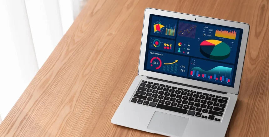 Laptop on a wooden desk displaying a colorful data analytics dashboard on its screen.