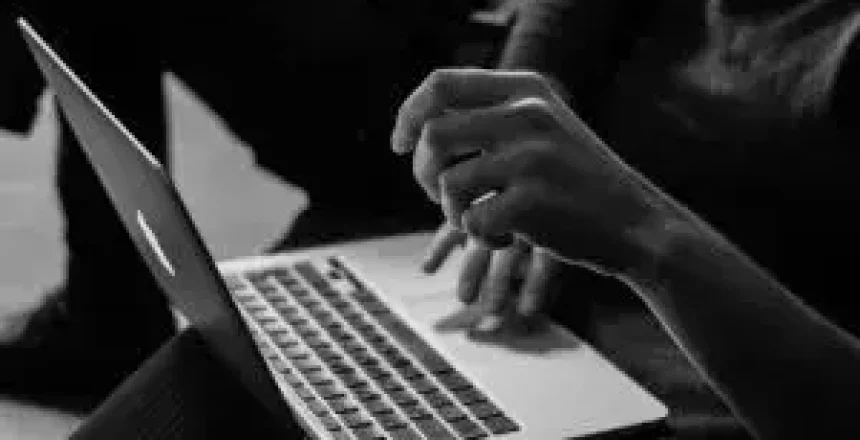 Person typing on a silver laptop resting on their lap (black-and-white photo).