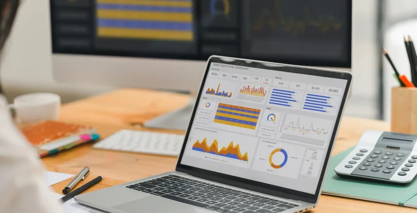 Laptop on a wooden desk displaying a colorful analytics dashboard with charts and graphs on screen.