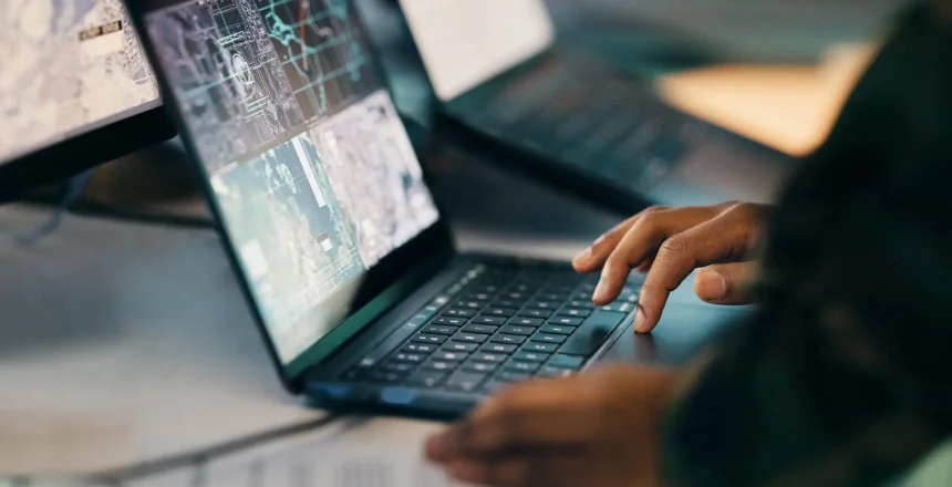 Hands typing, laptop and closeup on table of military intelligence, map and research on internet. Computer, soldier and veteran online for surveillance, cyber security and info of army professional