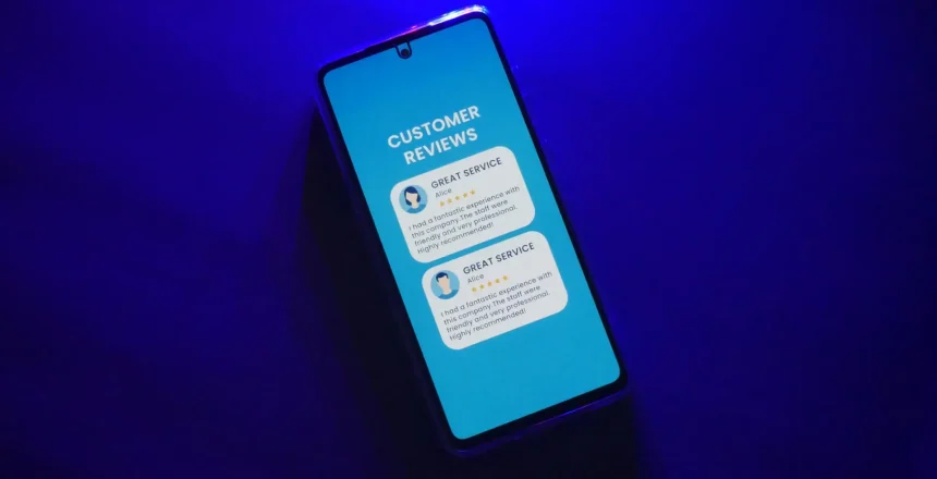 Smartphone on dark surface displaying customer review screen with five star ratings and positive service feedback illuminated blue light