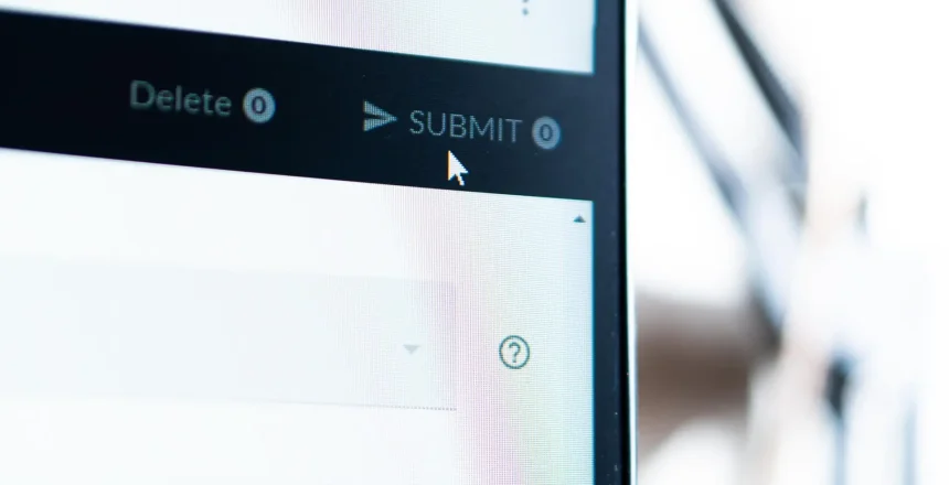 Close-up of a computer screen showing a SUBMIT button with a cursor hovering over it, indicating an action to be taken. The interface includes options like delete and language settings.