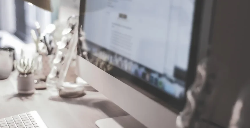 Blurred large computer screen on a home office desk interior eith work objects in background