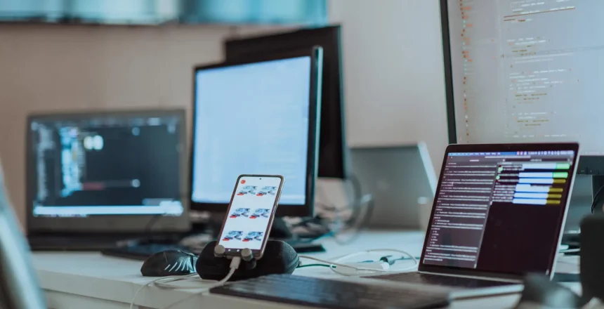 Computer screens running programming code in empty software developing agency office and computers parsing data algorithms in background. Neural network servers cloud computing in data room. High quality photo